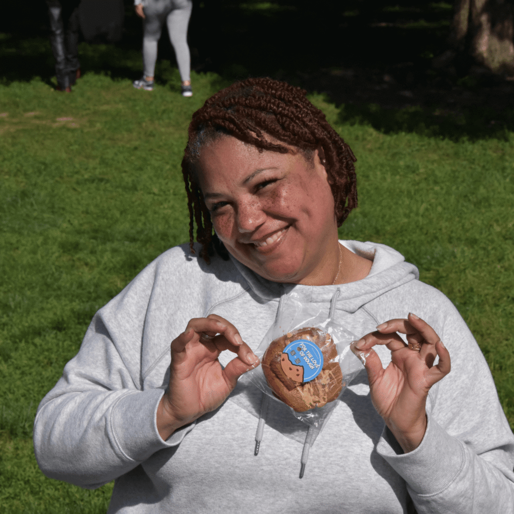 A woman holding a For the Love of Dough cookie smiling